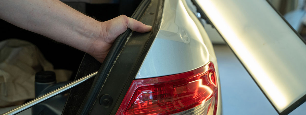 Paintless dent removal technicians hands with puller fixing dent on rear car bumper